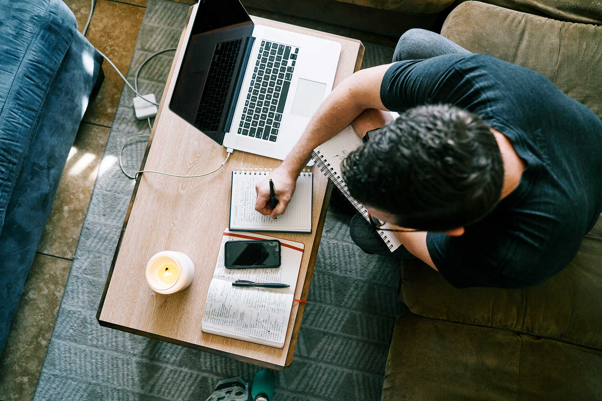 man writing in notebook next to computer